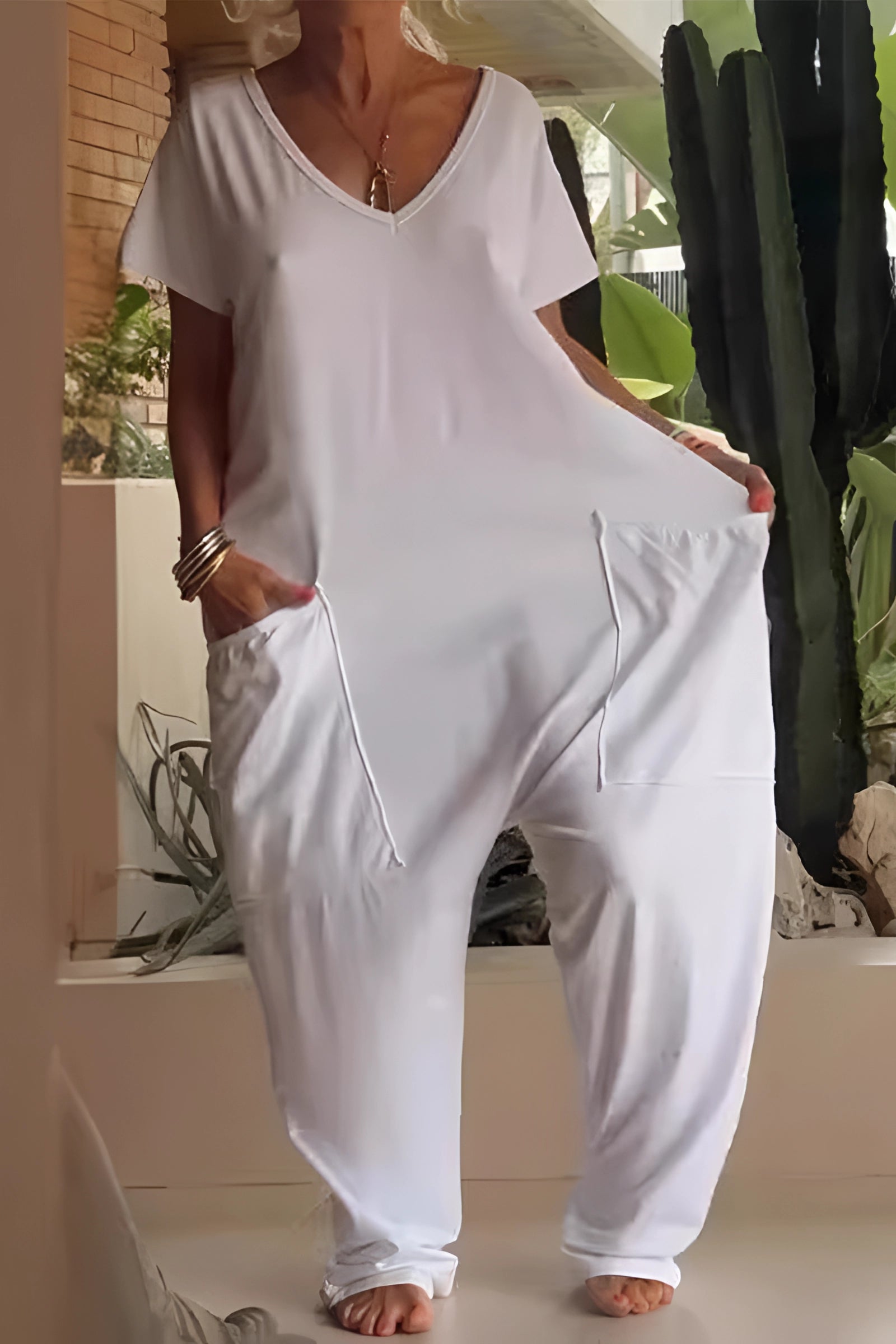 A woman wearing a white boho chic V-neck cotton oversized jumpsuit with pockets, featuring long sleeves and a relaxed fit.