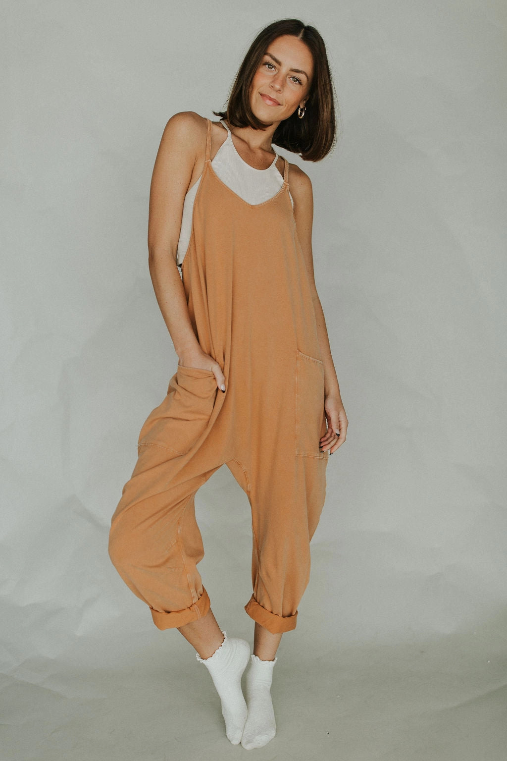 Woman smiling and wearing a light brown sleeveless loose-fit jumpsuit, showcasing the lightweight summer overalls design with comfortable fit around the waist, thigh, and knee.