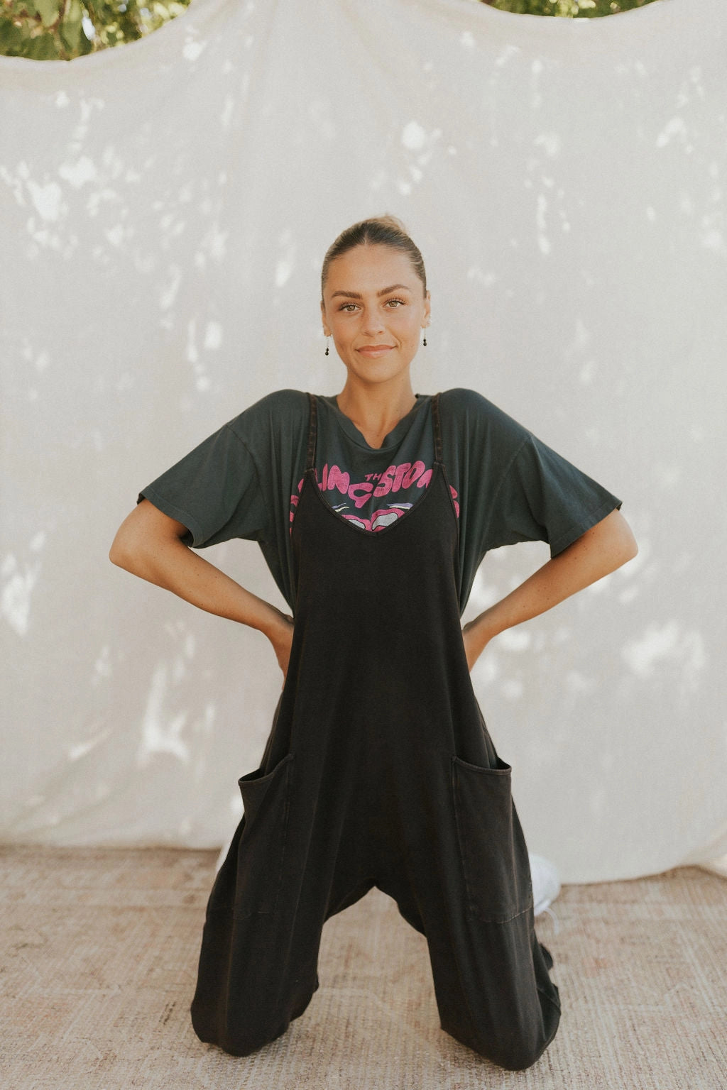 Woman smiling and wearing a camel sleeveless loose-fit jumpsuit, suitable for summer, standing on a tiled floor.