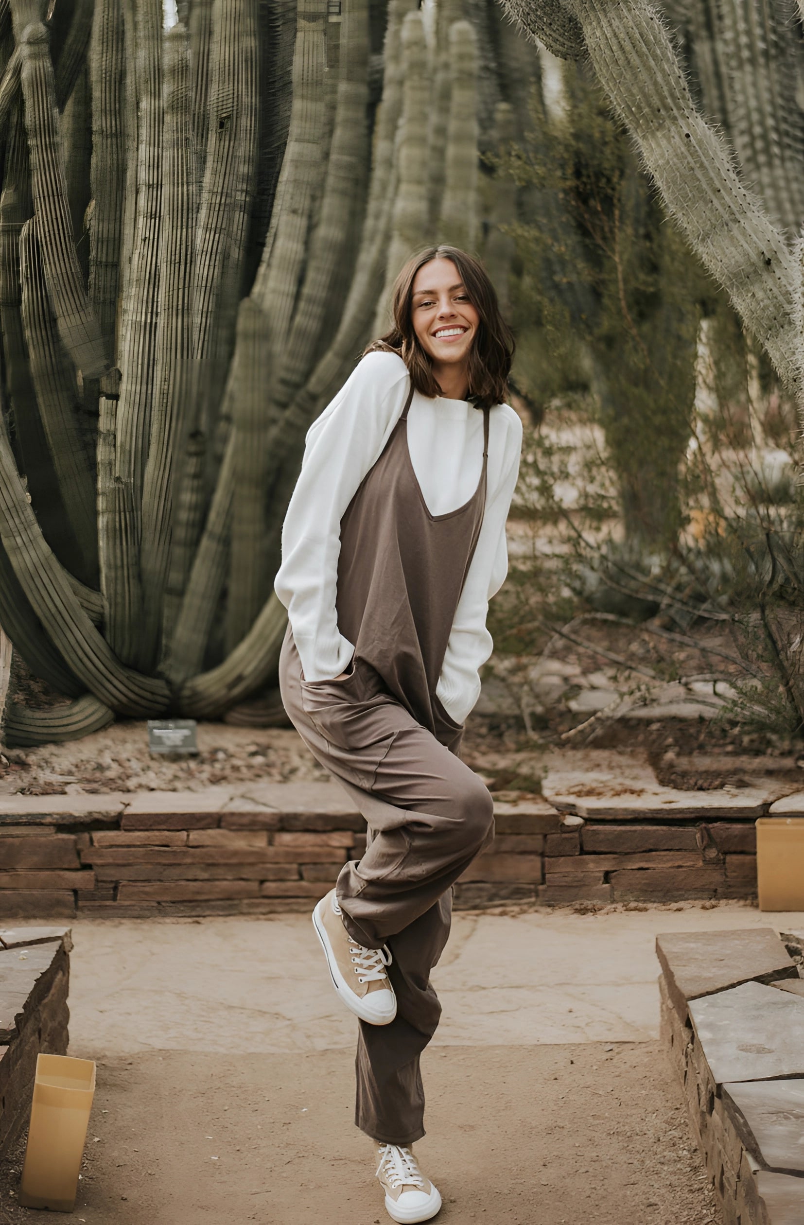 Woman wearing a camel sleeveless loose-fit jumpsuit, lightweight summer overalls, standing outdoors, smiling with casual hairstyle and shoes.